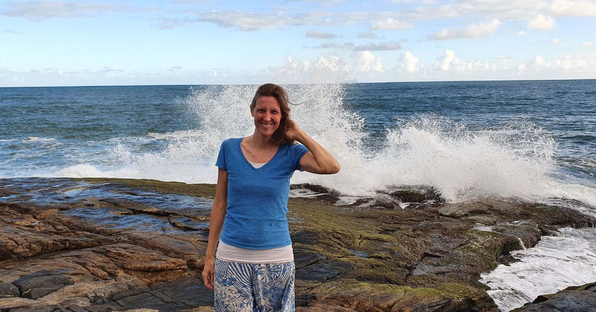Henriette steht auf den Klippen am Meer mit den Wellen, die hinter ihr hochschlagen